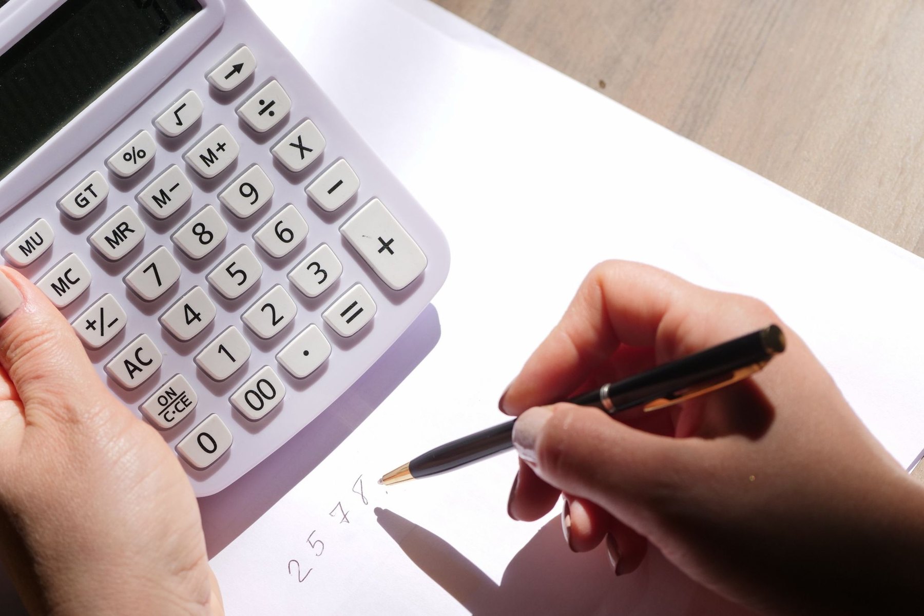 Hands using a calculator and pen to review figures